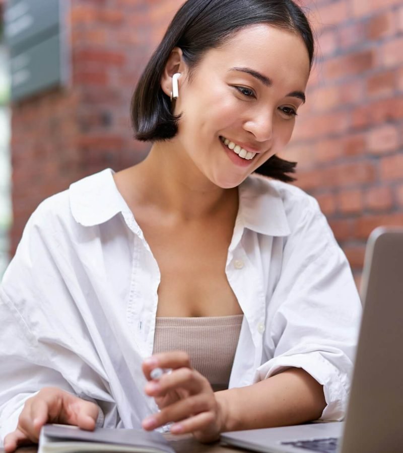 young-smiling-asian-woman-with-wireless-earphones-sitting-in-coworking-office-space-with-laptop.jpg